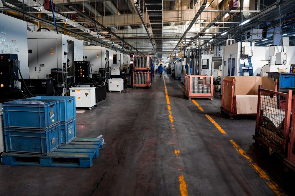 Chão de fábrica organizado, com máquinas, caixas e corredor demarcado