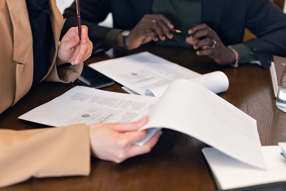 Mãos analisando documentos e currículos sobre uma mesa de reunião